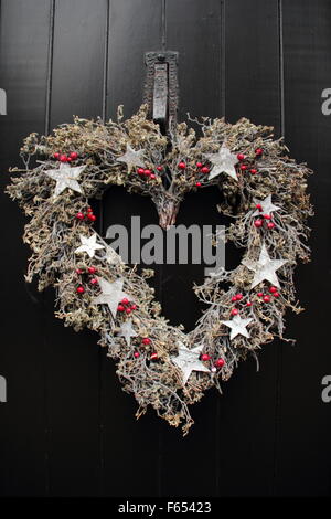 A rustic heart shaped Christmas garland,or wreath, hangs on a black wood door at a country cottage in the Peak District England Stock Photo