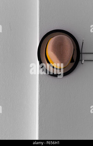 Hat hanging on a coat hanger mounted on a white plaster wall Stock Photo