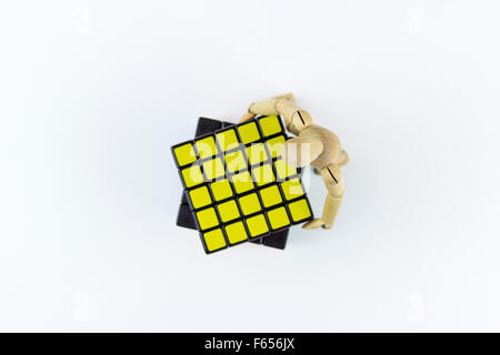 Wooden puppet trying to solve a puzzle cube, on a white background Stock Photo
