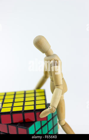 Wooden puppet trying to solve a puzzle cube, on a white background Stock Photo