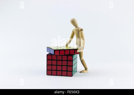 Wooden puppet trying to solve a puzzle cube, on a white background Stock Photo