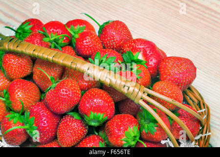 On the surface of the wooden table is a wicker basket filled with ripe red strawberries. Stock Photo