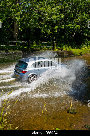 Car driving through a water filled ford crossing a stream on a country lane in England UK Stock Photo