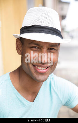 Head shot of any ethnic man smiling wearing a light blue green t-shirt and black and white fedora Stock Photo