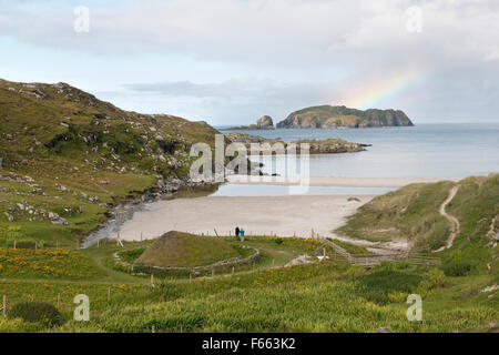 Tourists at replica Iron Age C6th-8thAD figure-of-eight house at head of Bosta beach, Great Bernera, Lewis, looking at rainbow over Seana Chnoc island Stock Photo