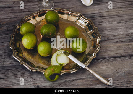 Limoncello in a classic elegant bottle and glass with green lemon on a silver serving plate with a knife Stock Photo