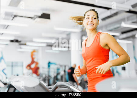 Beautiful young woman running on a treadmill in gym and smiling Stock Photo