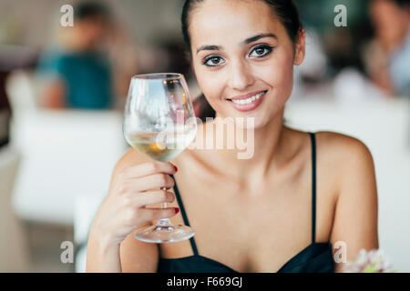 Woman tasting white wine in restaurant and lifting glass accordingly Stock Photo