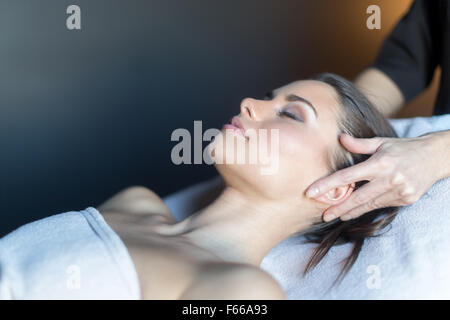 Masseur treating face of a beautiful, young woman lying on the massage table Stock Photo
