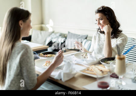 Two beautiful young women eating in a restaurant while having a conversation Stock Photo