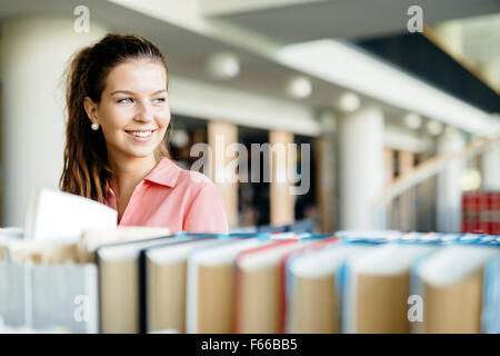 Beautiful female student takes the right book off the shelf Stock Photo