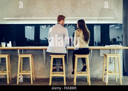 Young colleagues flirting in a bar and talking while sitting on chairs Stock Photo