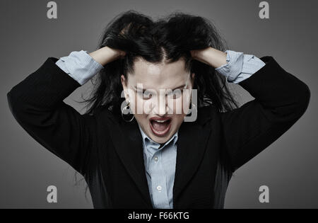 Toned closeup of an angry businesswoman pulling her hair and shouting, over gray background Stock Photo
