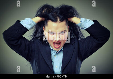 Closeup of an angry businesswoman pulling her hair and shouting, over gray background Stock Photo