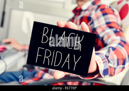 closeup of a young caucasian man wearing a plaid shirt sitting at his desk showing a black signboard with the text black friday Stock Photo