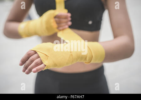 Close up of a young handsome caucasian brown hair woman wrapping her hands with a band, preparing herself for boxing training - Stock Photo