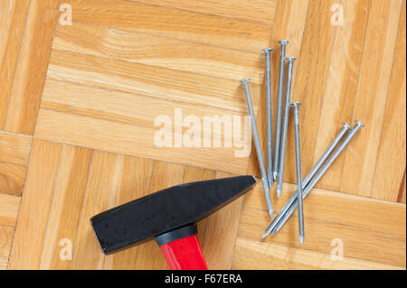 Black hammer and nails with flattened heads, unused objects group lying on the wooden parquet floor ready to use, domestic tools Stock Photo