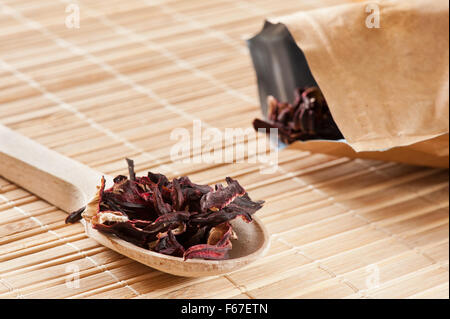 Dried Roselle Hibiscus sabdariffa petals tea portion lying on wooden spoon on mat, pile of red calyces or petals in horizontal Stock Photo
