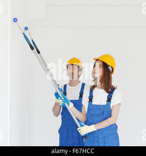Two workers in helmets painting wall with paint roller Stock Photo