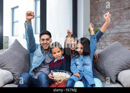 Happy young family eating popcorn while watching tv Stock Photo