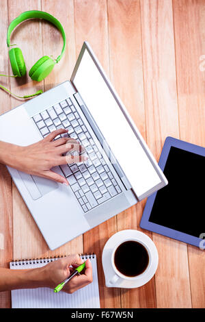 Overhead of feminine hand typing on laptop and taking notes Stock Photo