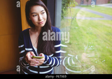 Smiling student with smartphone and looking through the window Stock Photo