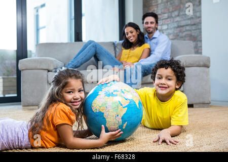 Children holding globe on carpet in living room Stock Photo