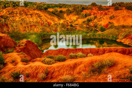 red soils around the freshwater lake formed in a former quarry for the extraction of bauxite in Italy Stock Photo