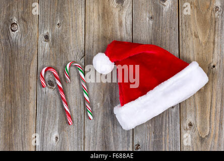 Traditional Christmas Santa cap and candy canes on rustic wood. Boards in vertical pattern. Stock Photo