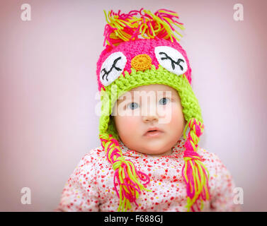 Portrait of beautiful little baby girl wearing stylish warm colorful knitted hat over pink background, winter children's fashion Stock Photo