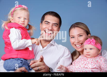 Portrait of happy family standing on blue clear sky background, parents with two adorable daughters having fun outdoors Stock Photo