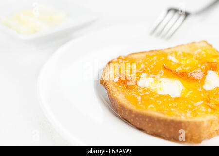 French toast with spread bitter orange marmalade or jam with candied peel, butter curls, fork on background and dishware on whit Stock Photo