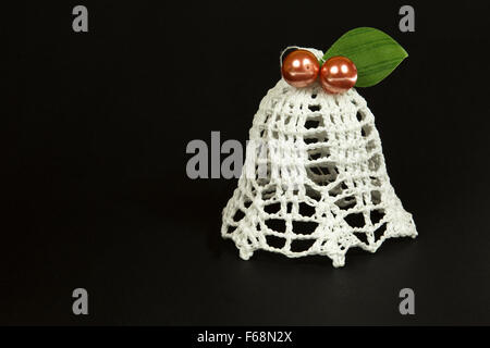 White bell, Christmas Tree ornament hand-made yarn with two red beads and a green leaf.isolated on a black background.Close,hori Stock Photo