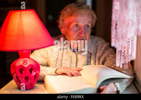 Elderly woman reads a book with a table lamp. Stock Photo
