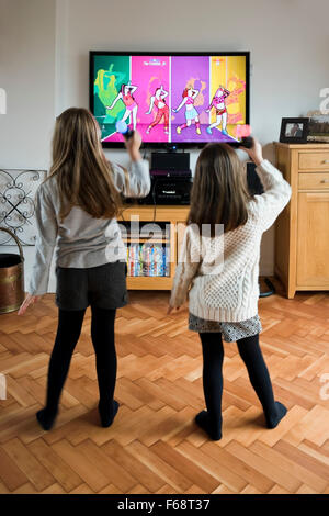 Vertical portrait of two little girls dancing and singing together on their games console. Stock Photo