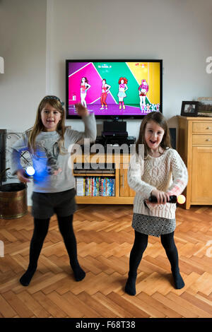 Vertical portrait of two little girls dancing and singing together on their games console. Stock Photo