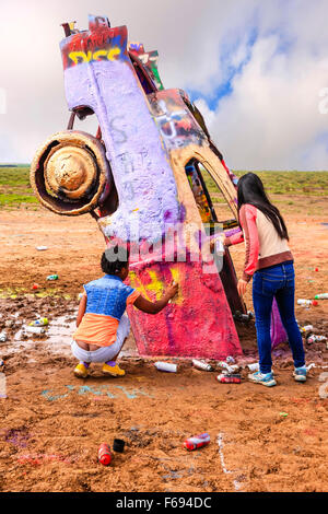 People adding their own art with spray cans of paint to the Cadillac Ranch public art sculpture in Amarillo, Texas. Stock Photo