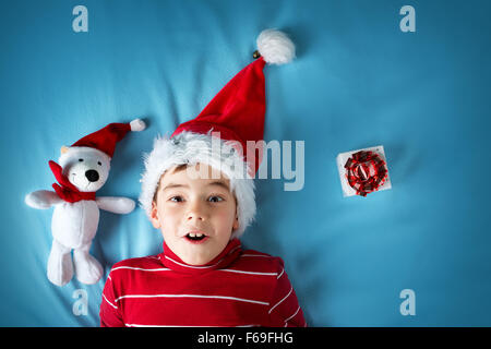 Happy boy in santa claus hat with a white bear on blue background Stock Photo