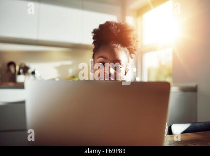 Smiling black girl with a cute hairstyle sitting at a laptop computer browsing the internet and her social media or working on h Stock Photo