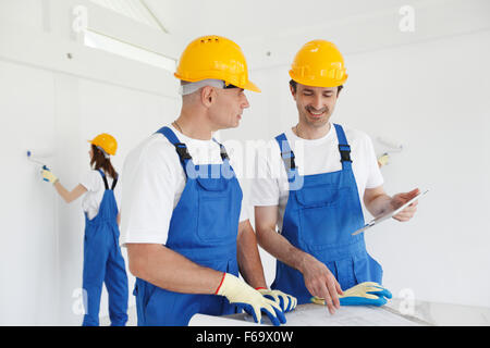 Construction workers looking at house plan and painting walls Stock Photo