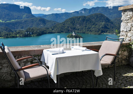 Served table with emty plate outdoor. View over lake Bled, island with church and Alps mountains in the background. Slovenia. Stock Photo
