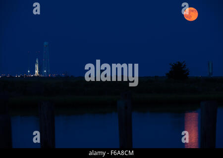 The image shows the full Moon rising beside the Antares rocket carrying the Cygnus spacecraft at Launch Pad-0A at NASA’s Wallops Flight Facility in Virginia on July 12, 2014, during preparations for the Orbital-2 cargo mission to the International Space Station. Stock Photo