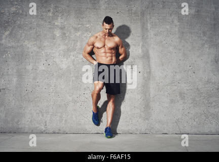 Fitness model standing against grey background, no shirt showing abdominal muscles, room for copy space, fitness concept adverti Stock Photo