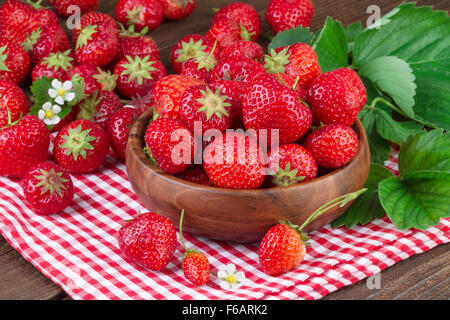 ripe strawberry in wooden bowl on red checkered tablecloth