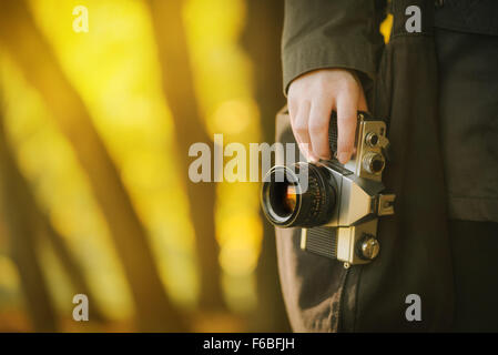 Hipster photographer exploring nature autumn scenery with old vintage film camera, retro toned image with selective focus