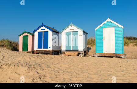 A row of clouful huts on a sandy beach backed by dunes at Southwold on the Suffolk coast Stock Photo