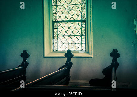 A dimly lit interior from a stained glass church window with carved crosses decoratively set on the ends of each wooden pew art Stock Photo