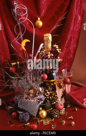 Festive New Year's, Christmas still life with a wine bottle champagne, two glasses and Christmas jewelry on a red background. Stock Photo