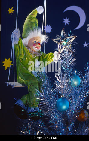 Festive New Year's, Christmas still life with a toy the clown attaches a star on a silver artificial Christmas Christmas tree. Stock Photo
