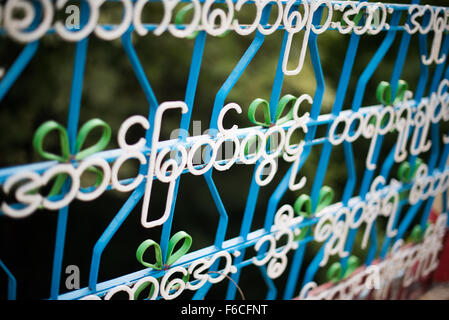 U Min Thonze Pagoda Burmese Script Ironwork Fence Detail Sagaing Myanmar | SAGAING, Myanmar — White-painted iron Burmese script is bent and welded into the bars of a blue metal fence marking a boundary at U Min Thonze Pagoda on Sagaing Hill. Burmese script's distinctive circular letterforms trace back to the practice of writing on palm leaves, where straight strokes would split the material, and the rounded characters lend themselves naturally to scrollwork and ironwork. The fence stands on the Sagaing Fault, which ruptured in a magnitude-7.7 earthquake in March 2025. Stock Photo